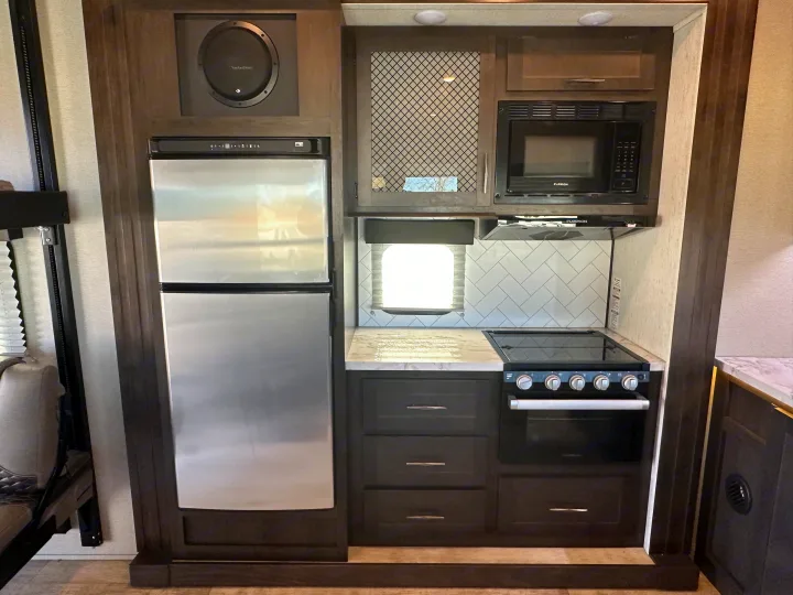 Explore this RV rental's full kitchen with stainless refrigerator, microwave, and stove for easy travel meals.. Grand Design Momentum 2022
