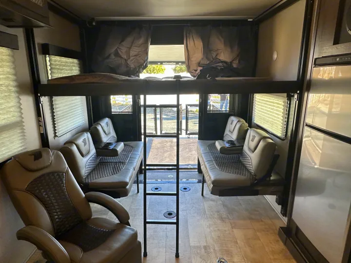 Spacious RV rental toy hauler interior with upper bunk, modular seating, and large rear ramp for gear.. Grand Design Momentum 2022