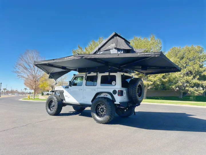 White Jeep Wrangler with a rooftop tent & large side awning deployed. An adventure vehicle, ideal as an RV rental alternative for camping.. Jeep Overlander 2019