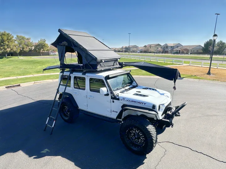 White Jeep with a deployed CHOTSE roof tent and side awning, perfect for an rv rental camping trip.. Jeep Overlander 2019