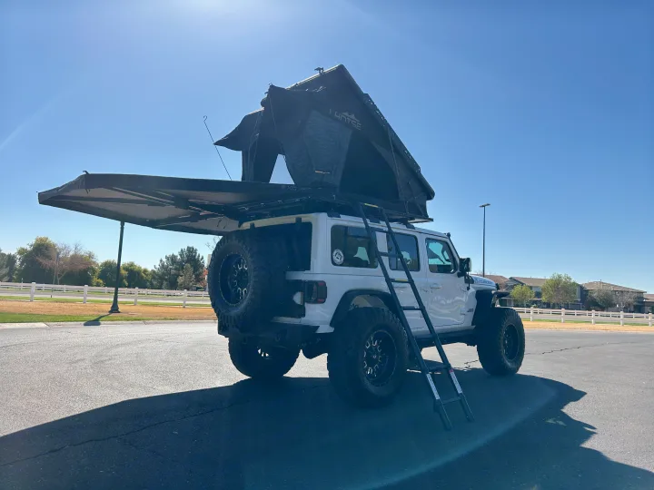 White Jeep with deployed rooftop tent and ladder, an adventurous RV rental for overland camping.. Jeep Overlander 2019