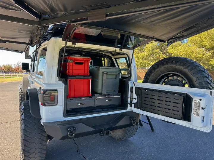 White Jeep Wrangler customized for overlanding: large awning, rear storage system with crates & fridge. Ideal for RV rental adventures.. Jeep Overlander 2019