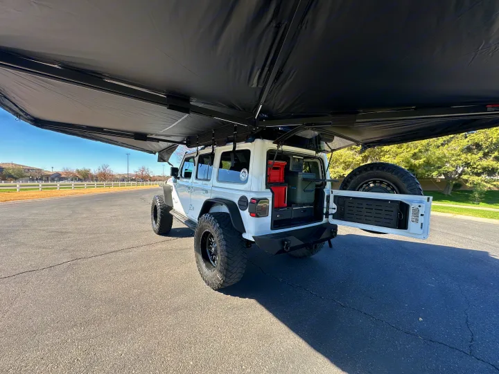 White Jeep with deployed awning and custom rear storage (cooler, crates). Ready for your next RV rental adventure!. Jeep Overlander 2019