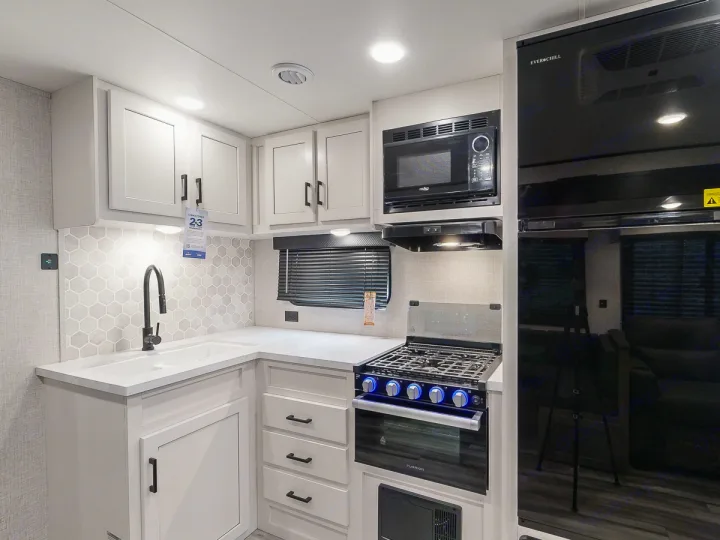 Modern rv rental kitchen with white cabinets, hex backsplash, black sink, stove, microwave, and Everchill fridge.. Jayco Jay Flight 2024