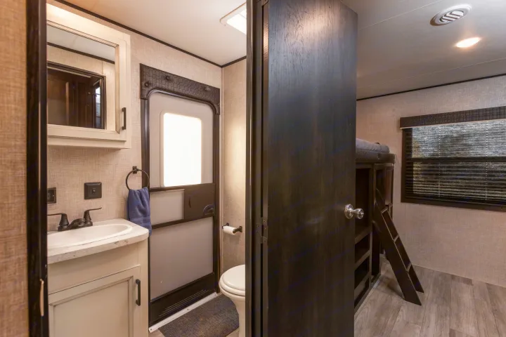 RV rental interior: compact bathroom with sink, toilet, RV entry door, and an open door to bunk beds.. Jayco Jayflight 32BHDS.G 2022