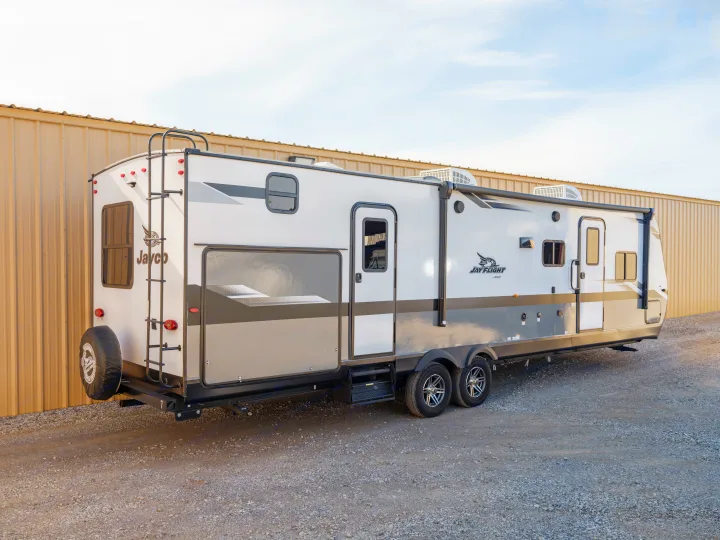 A white and gray Jayco Jay Flight travel trailer RV rental, parked on gravel next to a building, ready for your next adventure.. Jayco Jayflight 32BHDS.G 2022