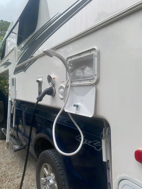Side of an RV rental: external shower, power, and water hookups on a white truck camper over a blue pickup. Ready for use.. Northern Lite 9-6 Wet Bath 2022