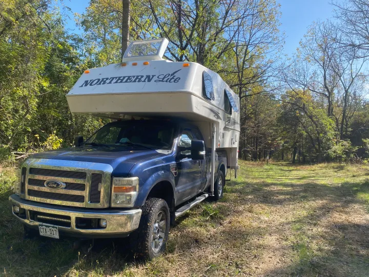 Blue Ford truck with a white Northern Lite truck camper, an RV rental, parked in a sunny outdoor clearing.. Northern Lite 9-6 Wet Bath 2022