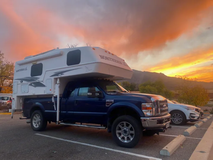 A blue F-350 pickup with a white Northern Lite truck camper, parked at sunset near mountains. Ideal for an RV rental getaway.. Northern Lite 9-6 Wet Bath 2022