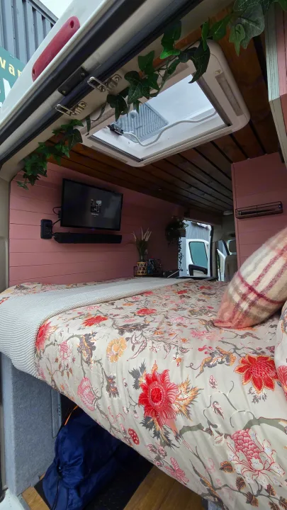 Explore this cozy RV rental's interior: floral bed, TV, skylight, and pink walls for adventures.. Citroen Relay L3H2