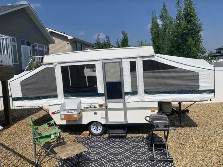 Enjoy a pop-up RV rental experience! Camper set up with a grill & seating for outdoor living on a sunny day.. Forest River Palomino 2000