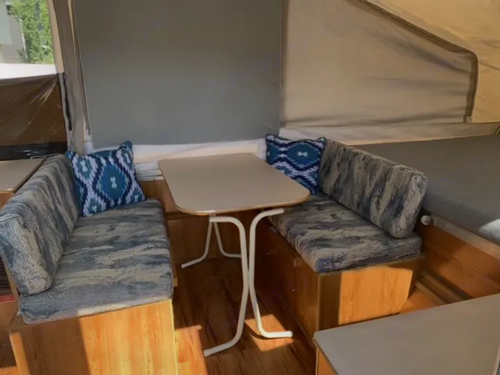 This RV rental's dinette features patterned benches, a white table, and blue pillows in a cozy camper interior.. Forest River Palomino 2000