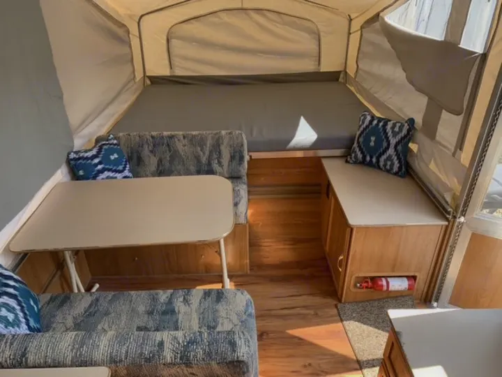 This pop-up RV rental interior shows a dining area, beds, and a fire extinguisher for safe travel.. Forest River Palomino 2000