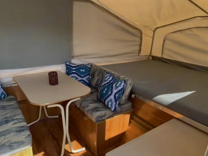 Inside a pop-up camper for rv rental, featuring a cozy dining area and bed. Enjoy comfortable adventures!. Forest River Palomino 2000