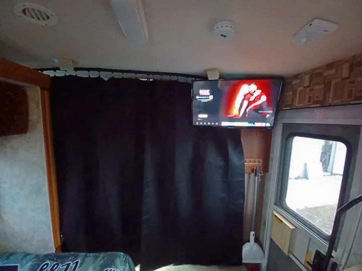 Inside an RV rental: TV displaying a video, ceiling fixtures, and a black privacy curtain dividing the space.. Winnebago Outlook 2007