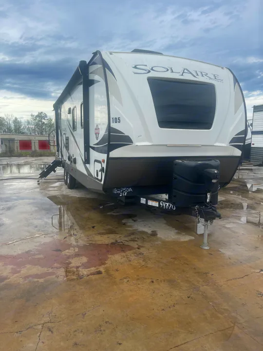 White Solaire travel trailer RV rental, parked on a wet lot, showing the front and side view.. Palomino Solaire Ultra Lite 2020