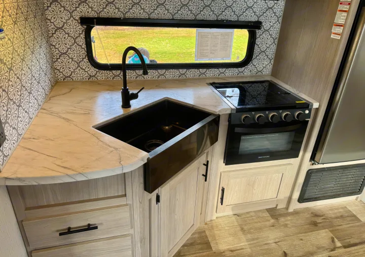 Modern RV rental kitchen with black farmhouse sink, sleek oven, light wood cabinets, and stylish backsplash.. Coleman Lantern 2022