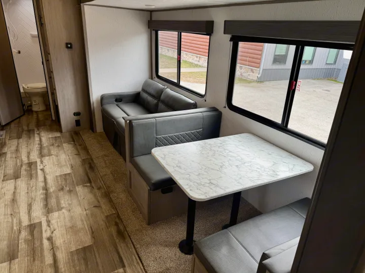 Inside an RV rental: a gray sofa, dinette with a white marble-look table, and wood-look flooring. Bathroom entrance visible.. Coleman Lantern 2022