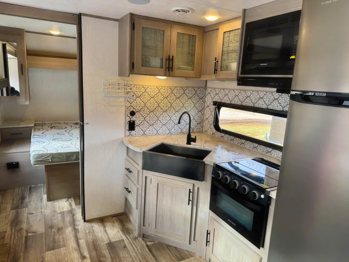 RV rental interior: full kitchen with black farmhouse sink, stove, microwave, fridge, patterned backsplash, and cozy bed.. Coleman Lantern 2022