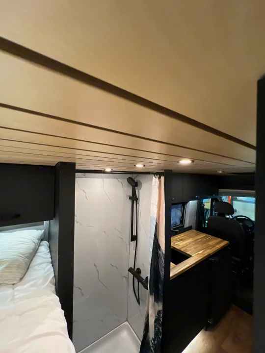 Explore this modern RV rental: comfy bed, sleek shower, and wood kitchen inside a compact, well-designed camper van.. Dodge Sportsman 2025