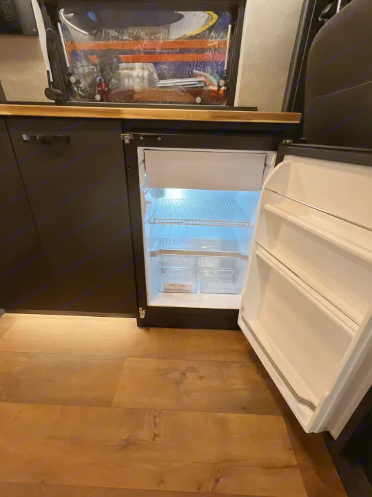 RV rental: Bright, open built-in refrigerator with storage bins, part of a compact kitchen setup in a camper.. Dodge Sportsman 2025