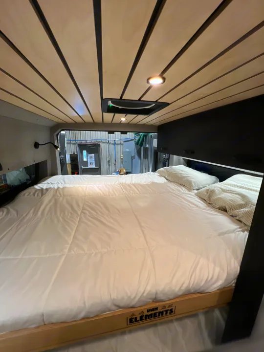 This RV rental features a cozy sleeping area with a comfortable bed, wood-slat ceiling, and practical overhead storage.. Dodge Sportsman 2025