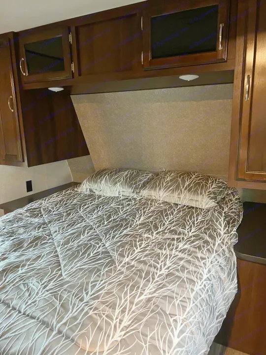 Cozy RV rental bedroom features dark wood cabinets, modern lighting, and a bed with a unique white branch patterned comforter.. Jayco Jay Flight 2018