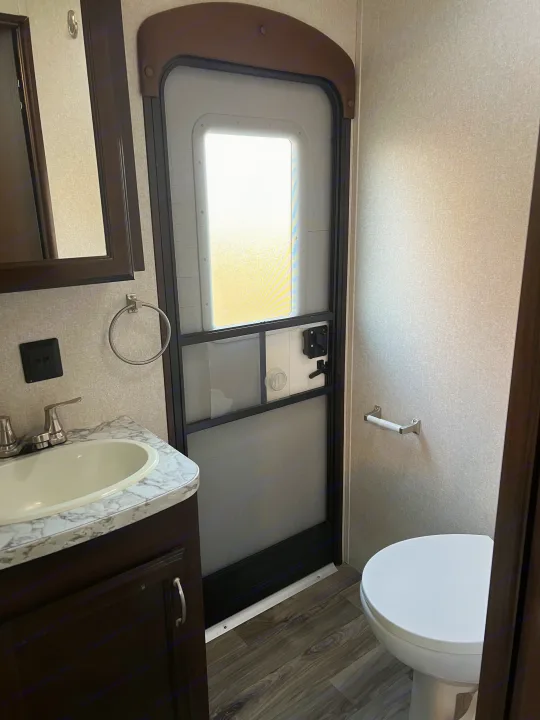 Inside an RV rental, a compact bathroom features a sink, toilet, and the main entry door with a bright window.. Jayco Jay Flight 2018