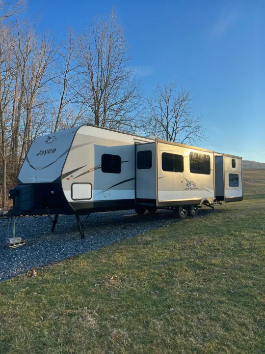 A Jayco Jay Flight travel trailer rv rental, fully extended & set up on gravel, ready for camping under a clear sky.. Jayco Jay Flight 2018