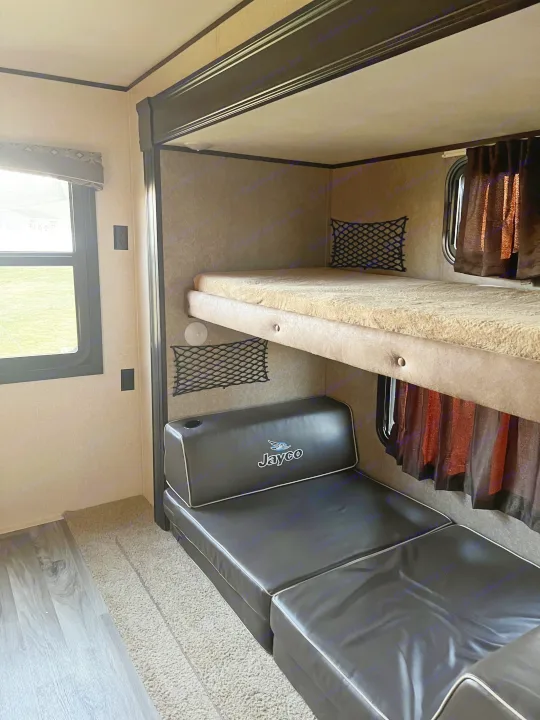 Inside an RV rental: a flexible space featuring comfortable bunk beds and a black convertible sofa below, ideal for resting or lounging.. Jayco Jay Flight 2018
