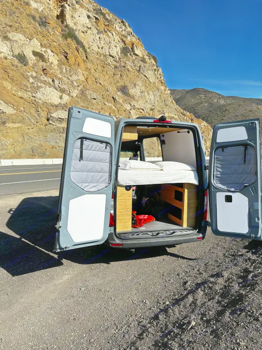 This RV rental van, with its cozy bed revealed, is parked on a scenic mountain road. Perfect for travel adventures!. Mercedes-Benz Sprinter 2024