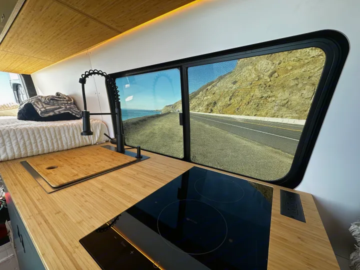 Stunning RV rental interior with kitchen, bed, and ocean road view from the window. Perfect for van life adventures!. Mercedes-Benz Sprinter 2024