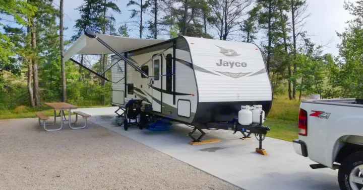 A Jayco RV is parked at a scenic campsite with a picnic table and truck, ready for your next RV rental adventure.. Jayco Jay Flight SLX 2019