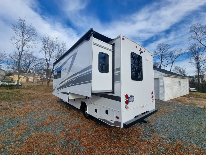 A modern white Entegra Coach RV rental with slide-out extended, parked on gravel amidst bare trees under a blue sky.. Entegra Qwest SE 2025 Qwest 2025 Mercdes-Benz 2025
