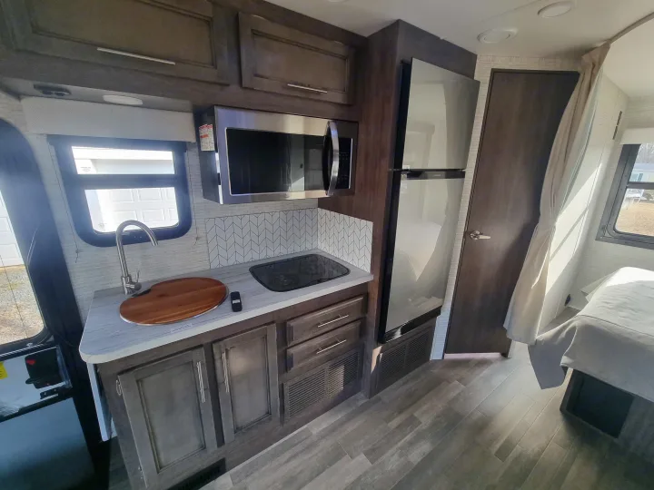 Compact RV rental kitchen with microwave, sink, and stovetop, plus refrigerator and a cozy bedroom beyond.. Entegra Qwest SE 2025 Qwest 2025 Mercdes-Benz 2025
