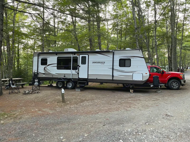 A full campsite setup with an Innsbruck RV rental travel trailer and red pickup truck surrounded by trees.. Gulf Stream Innsbruck 2014