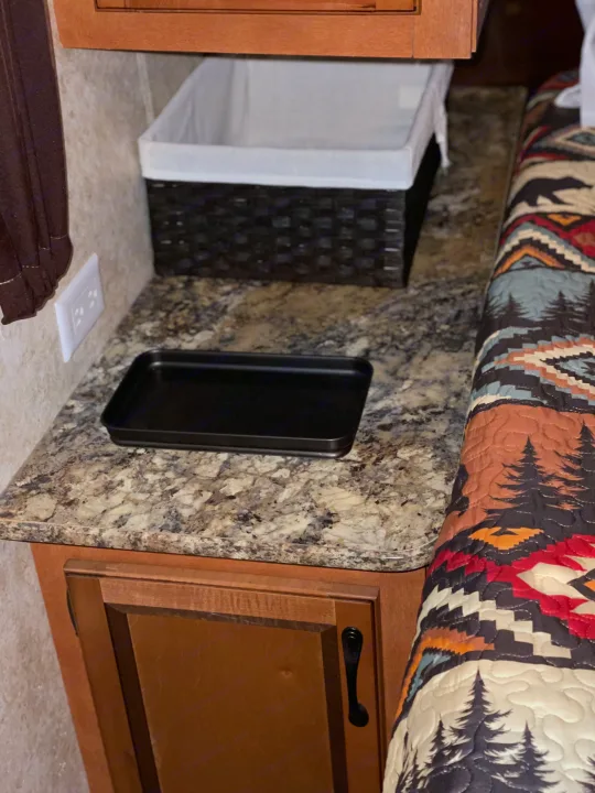 Cozy RV rental bedroom counter with storage basket, outlet, and a rustic quilt. Perfect for compact living.. Gulf Stream Innsbruck 2014
