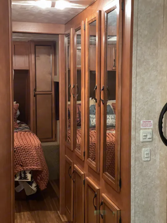 Cozy RV rental interior featuring a bedroom with a chunky knit blanket, wooden cabinetry, and mirrored wardrobe doors.. Gulf Stream Innsbruck 2014