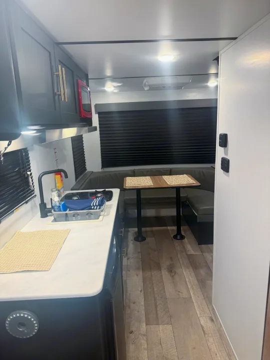Modern RV rental interior with a sleek kitchen, U-shaped dinette, and wood-look flooring, offering comfort for travel.. Forest River Wildwood FSX 2022