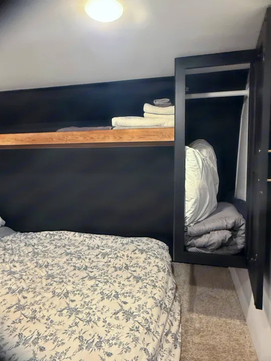 Inside an RV rental: a cozy bedroom with a floral bed, dark walls, and smart integrated shelving for essentials.. Forest River Wildwood FSX 2022