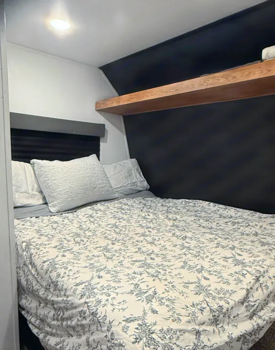 Inviting RV rental bedroom: patterned bed, white/gray decor, built-in shelf, and dark headboard wall for your trips.. Forest River Wildwood FSX 2022