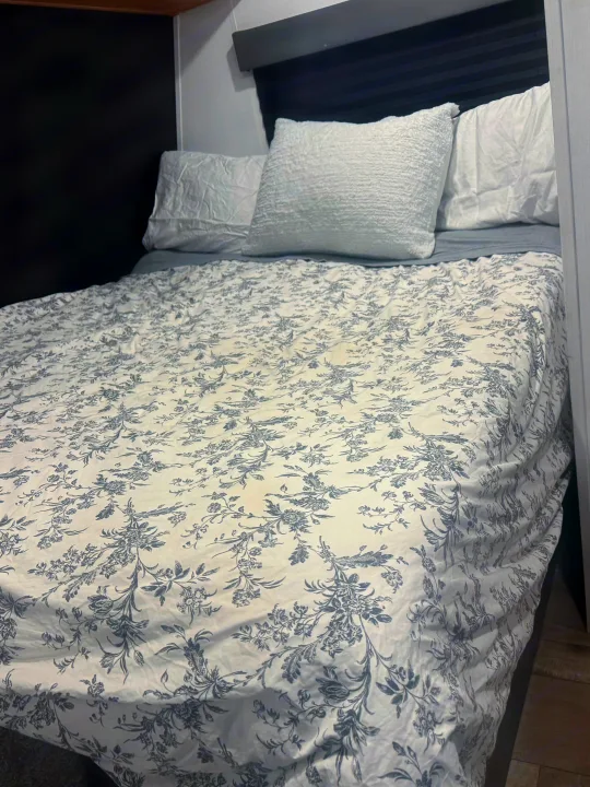 RV rental bedroom: A neatly made bed with white and gray floral bedding and white pillows, against dark and light walls.. Forest River Wildwood FSX 2022