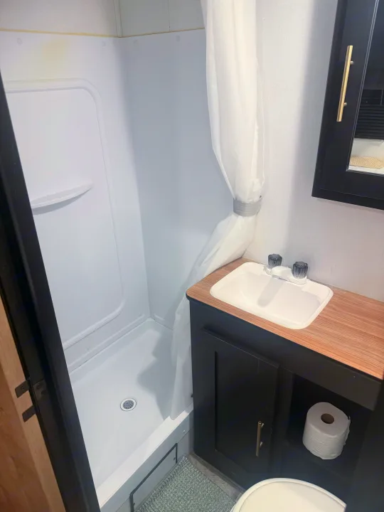 Explore this compact rv rental bathroom, featuring a white shower, sink, and vanity with a toilet area. Efficient and functional.. Forest River Wildwood FSX 2022