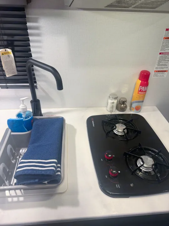 RV rental compact kitchen counter with sink, two-burner stove, PAM spray, and cooking essentials.. Forest River Wildwood FSX 2022