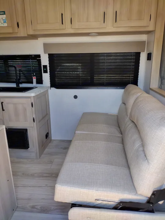 RV rental interior featuring a bright kitchen with a modern sink, light wood cabinets, and a neutral-toned sofa bed.. East to West Della Terra LE 2024