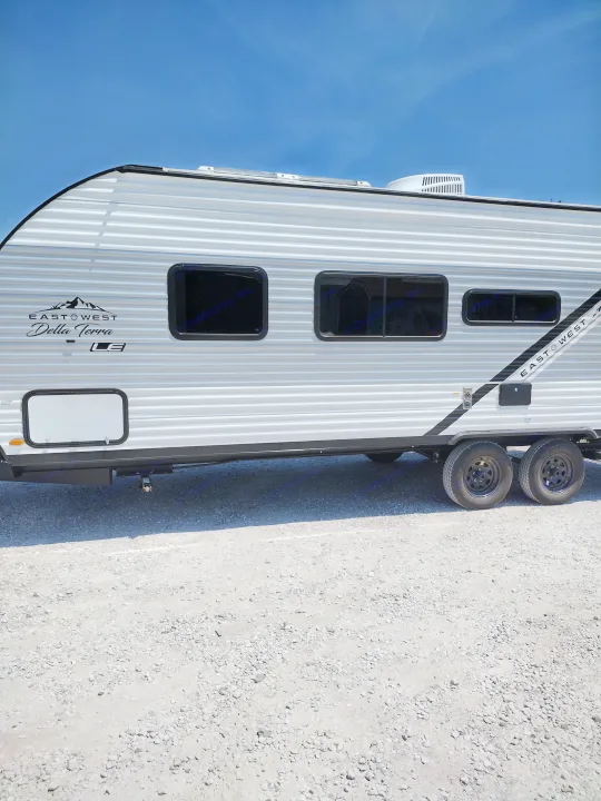 Side view of a white East West Della Terra LE travel trailer RV rental, with dark windows, parked on gravel.. East to West Della Terra LE 2024