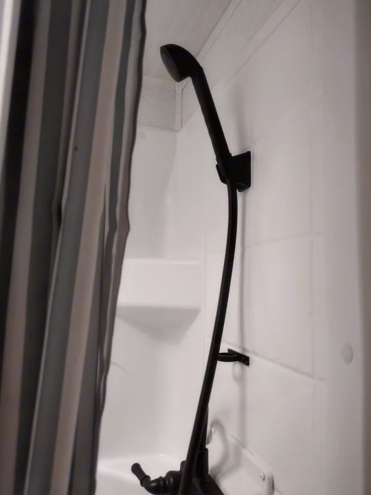Sleek, modern shower inside an RV rental, featuring black fixtures, white walls, and a striped curtain.. East to West Della Terra LE 2024
