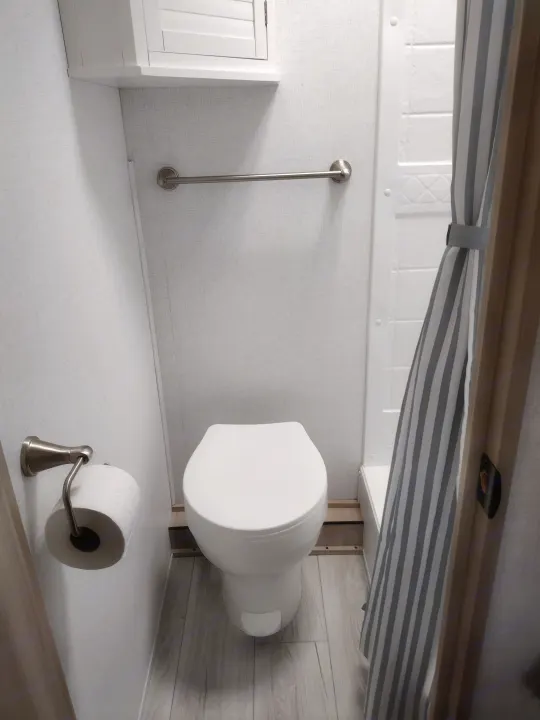 Compact RV rental bathroom features toilet, striped shower, towel bar, and TP holder for efficient space use.. East to West Della Terra LE 2024