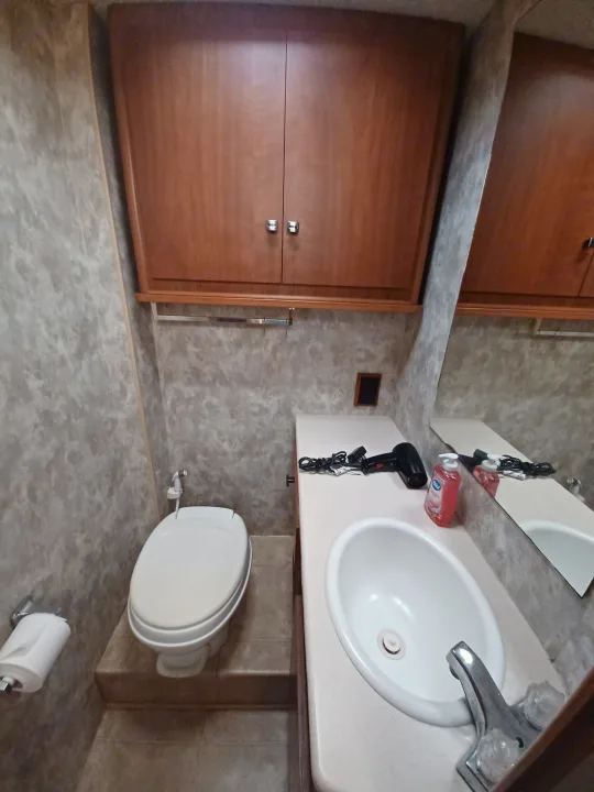 This compact RV rental bathroom features a toilet, sink, vanity, mirror, and wooden storage cabinets.. Winnebago Outlook 2007