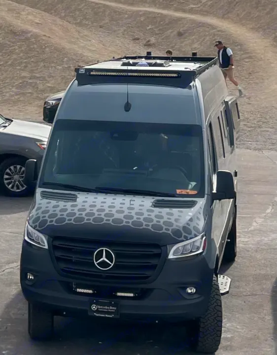 Custom gray Mercedes Sprinter van, an rv rental, with patterned hood and roof access, people visible on top.. Off Highway Van Off Highway Van Class B 2024